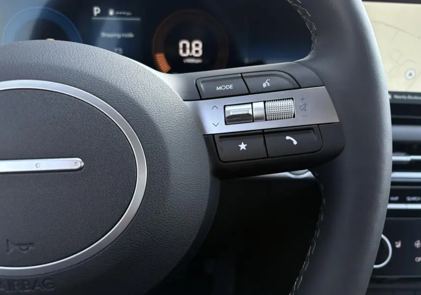 Gros plan sur le volant cuir noir du Hyundai Tucson 2025, avec commandes multimédia et tableau de bord numérique en arrière-plan.