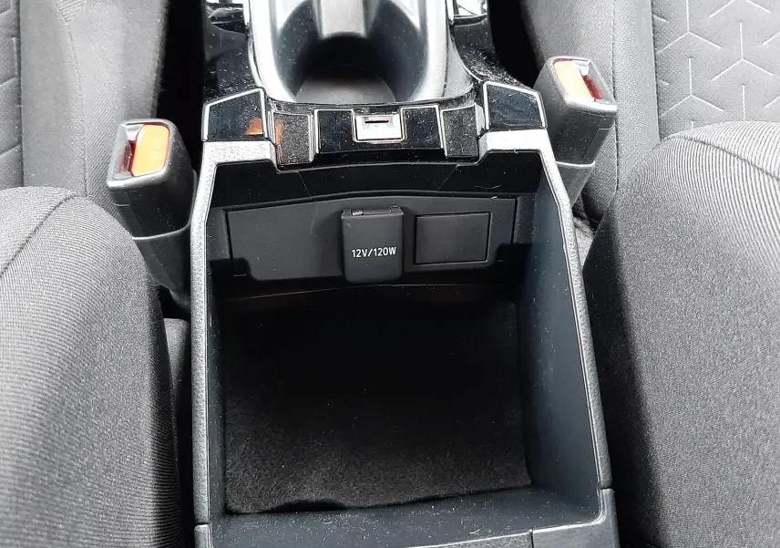 Vue plongeante sur la console centrale noire de la Toyota Corolla blanche 122 CH Dynamic, avec prise 12V visible entre les sièges en tissu gris.