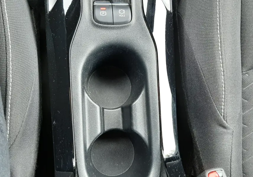 Gros plan sur la console centrale noire de la Toyota Corolla blanche 2022, avec porte-gobelets et boutons de frein à main électronique.