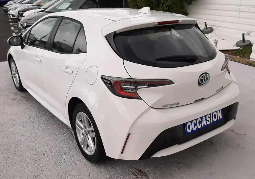Vue 3/4 arrière droite d'une Toyota Corolla blanche hybride 2022 avec hayon et feux arrière LED, en stationnement.