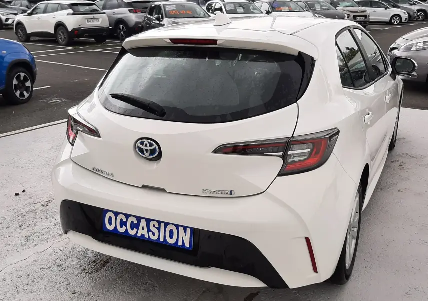 Vue 3/4 arrière droite d'une Toyota Corolla blanche hybride 2022 avec plaque "OCCASION" sur parking.