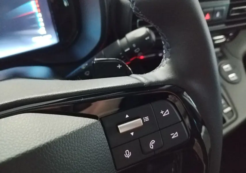 Gros plan sur les commandes multifonctions noires du volant du Citroën Berlingo 2025, intérieur sombre.