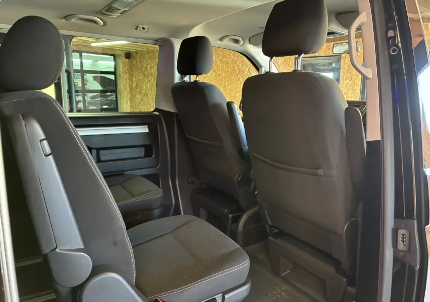 Intérieur noir du Volkswagen Multivan T6, vue arrière côté droit sur les sièges et la porte ouverte.