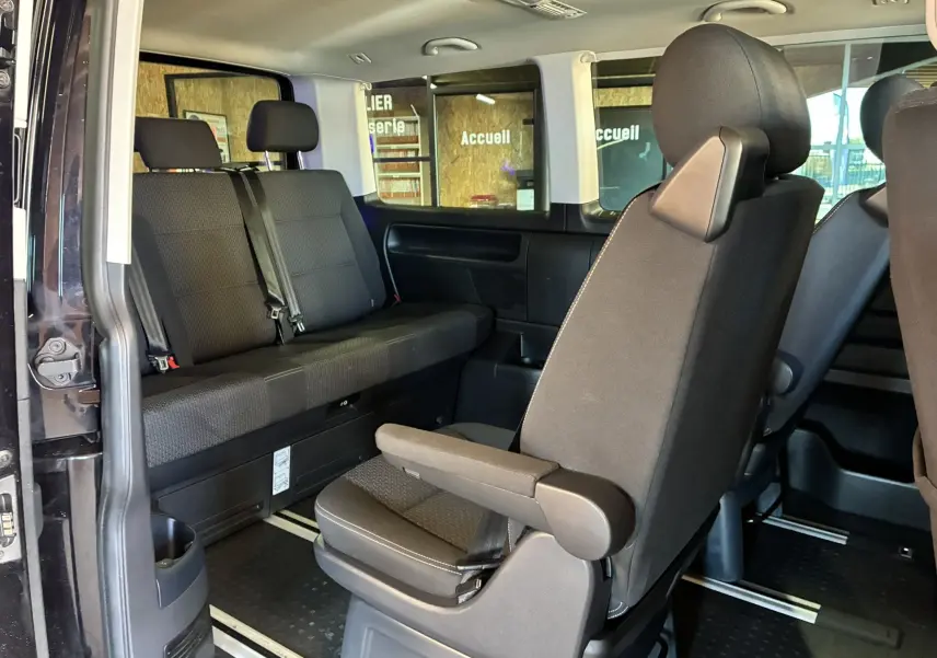 Vue intérieure côté gauche du Volkswagen Multivan T6 noir, montrant les sièges arrière et une banquette trois places.