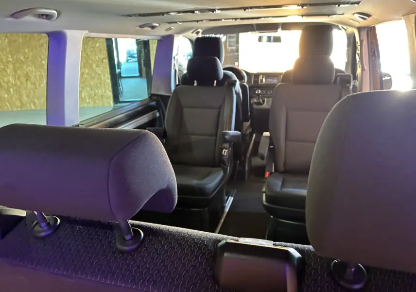 Intérieur du Volkswagen Multivan T6 PH.1 noir, vue depuis l'arrière montrant les sièges avant et milieu en tissu noir.