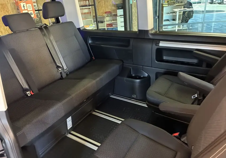 Vue intérieure côté droit du Volkswagen Multivan T6 PH.1 noir, montrant les sièges arrière et latéraux en tissu noir.