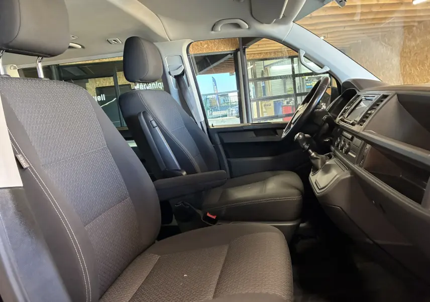 Vue intérieure côté conducteur du Volkswagen Multivan T6 PH.1 noir, montrant les sièges avant et la console avec boîte manuelle.