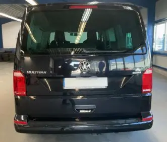 Volkswagen Multivan T6 noir vu en 3/4 avant droit dans un garage avec mur en bois et néon bleu.