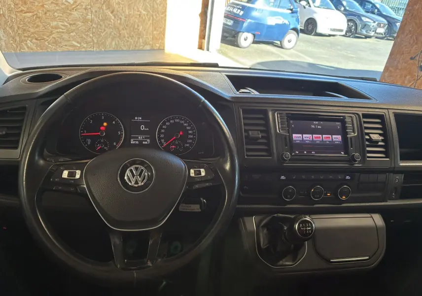 Vue intérieure centrée sur le volant noir et le tableau de bord du Volkswagen Multivan T6 avec boîte manuelle et écran tactile.