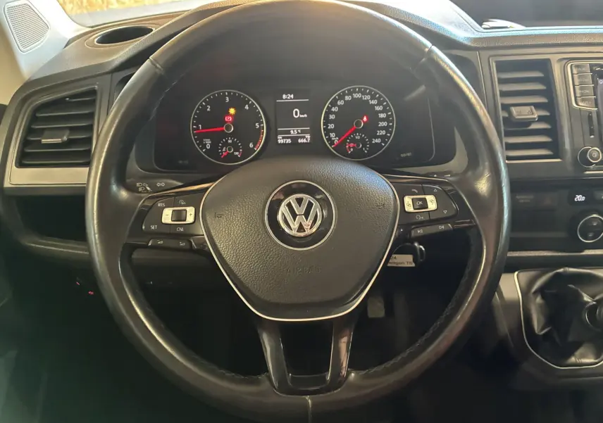 Vue rapprochée du volant noir de Volkswagen Multivan T6 avec tableau de bord et commandes visibles en arrière-plan.