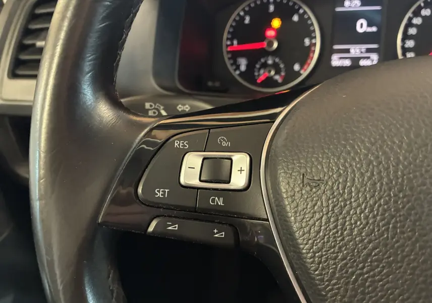 Gros plan sur les commandes de régulateur de vitesse au volant noir du Volkswagen Multivan T6 PH.1 2015, tableau de bord en arrière-plan.