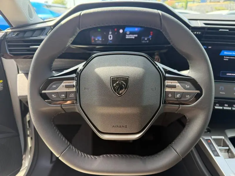 Vue rapprochée du volant noir de la Peugeot 308 1.2 Hybrid 145ch Allure 2025 avec logo lion central et commandes intégrées.