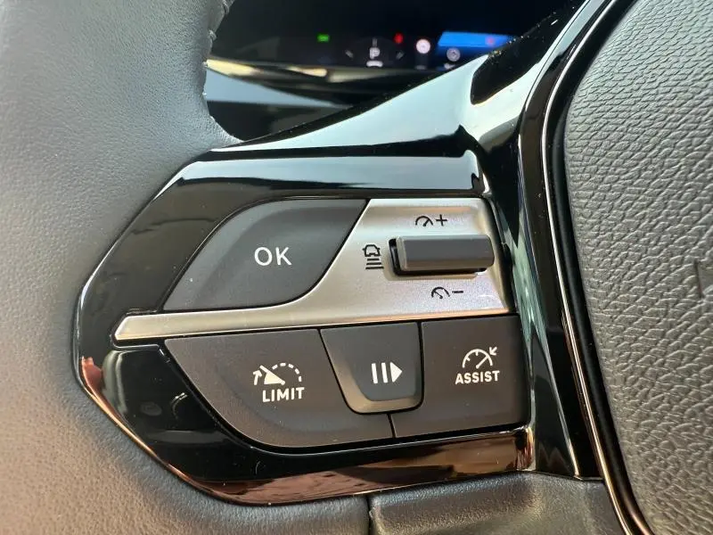 Gros plan sur les commandes au volant côté gauche de la Peugeot 308 blanche, avec boutons OK, LIMIT et ASSIST visibles.