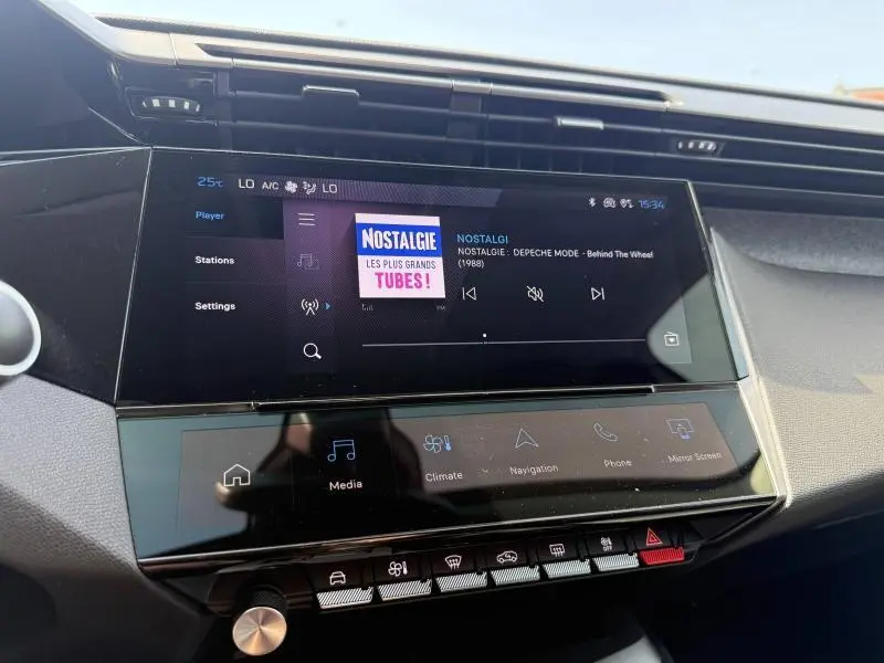 Écran tactile central du tableau de bord de la Peugeot 308 blanc Okénite, affichant la radio Nostalgie en mode hybride.