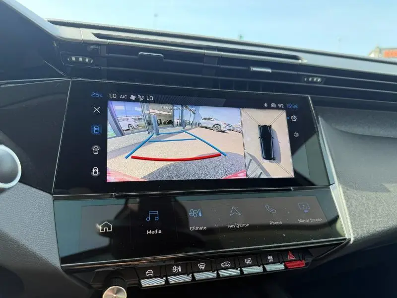 Écran central de la Peugeot 308 Hybrid 2025 montrant la caméra de recul avec vue arrière et vue aérienne du véhicule blanc Okénite.