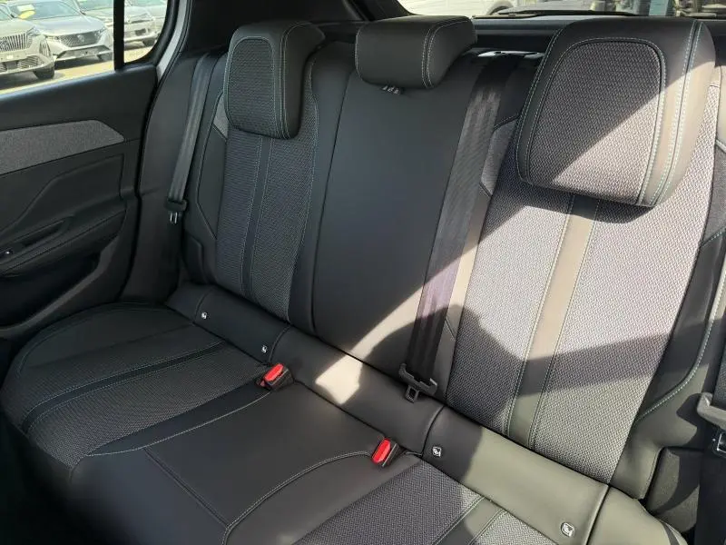 Vue intérieure des sièges arrière noirs en tissu et cuir du Peugeot 308 Hybrid 2025, avec appuie-têtes et ceintures visibles.
