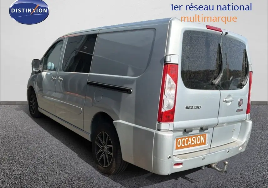 Vue 3/4 arrière droite d’un FIAT Scudo Fourgon gris métal avec hayon arrière vitré et attelage visible.