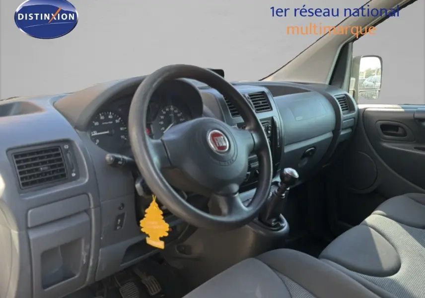 Vue intérieure côté conducteur du Fiat Scudo Fourgon gris métal, montrant le volant, tableau de bord et sièges tissu.