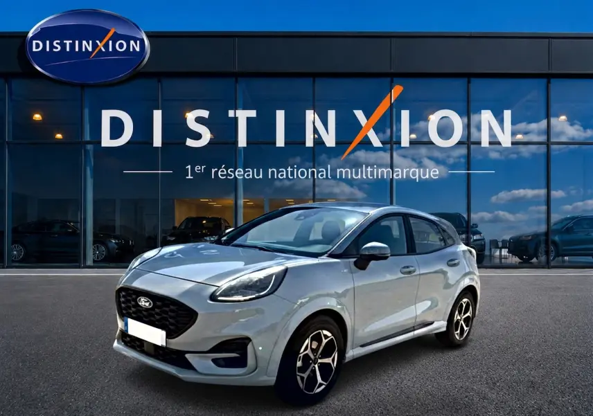 Ford Puma gris cactus en 3/4 avant droit, avec jantes alu et calandre noire, devant une vitrine Distinxion.