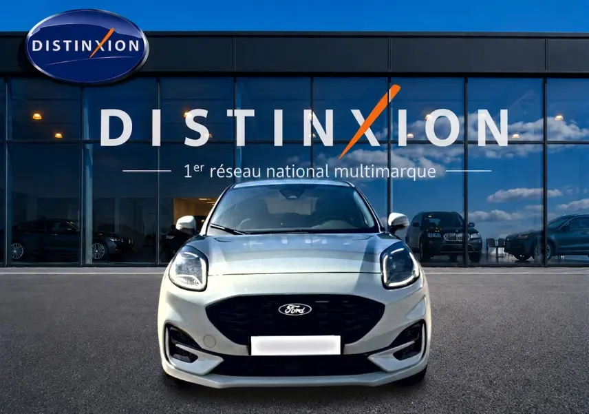 Vue frontale d'un Ford Puma gris cactus avec calandre noire et phares LED, devant une vitrine Distinxion.