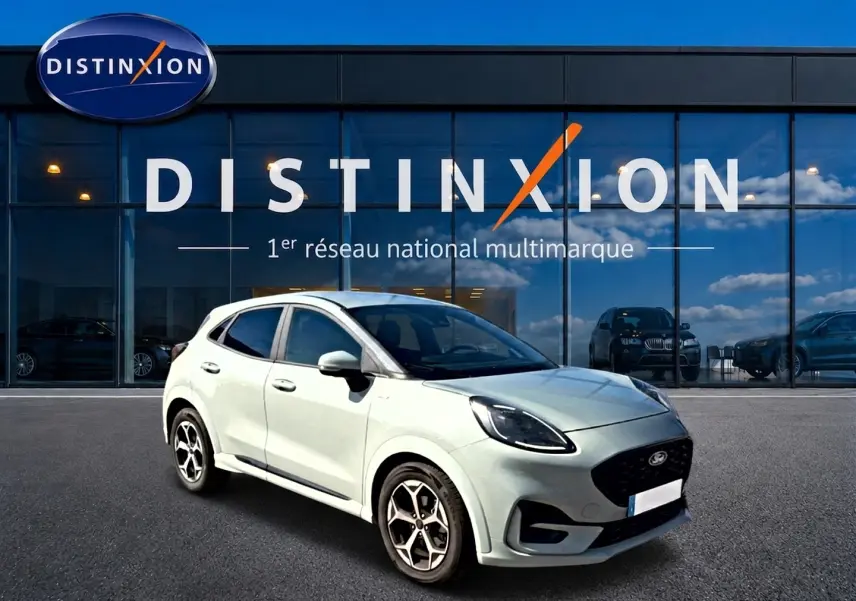 Ford Puma gris cactus en 3/4 avant droit, avec jantes alu et calandre noire, devant une vitrine Distinxion.