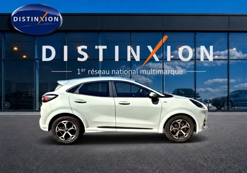Vue de profil côté gauche du Ford Puma gris cactus garé devant une vitrine avec logo Distinxion.