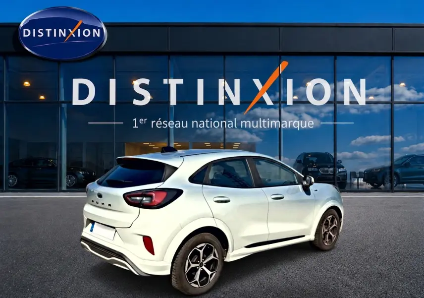 Vue 3/4 arrière droite d'une Ford Puma gris cactus 2025 devant une vitrine Distinxion, jantes alu visibles.