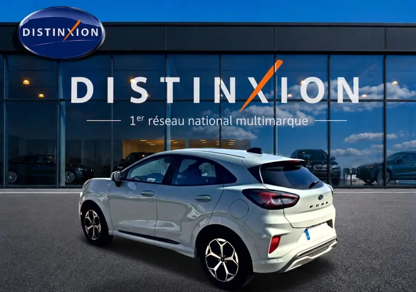 Ford Puma gris cactus vue 3/4 arrière droit, avec jantes alu et vitres arrière surteintées devant un showroom Distinxion.