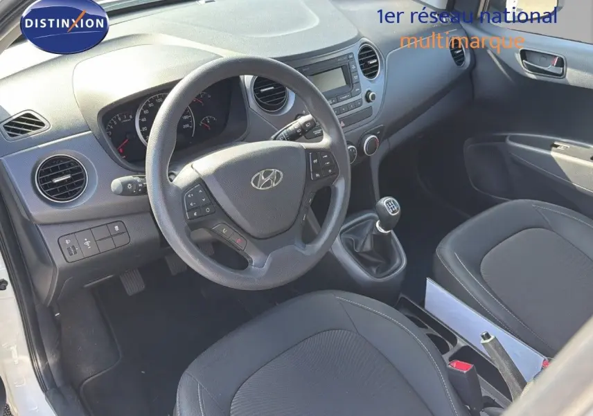 Vue intérieure côté conducteur de la Hyundai i10 blanche 2018, volant multifonction et levier de vitesses manuel visibles.