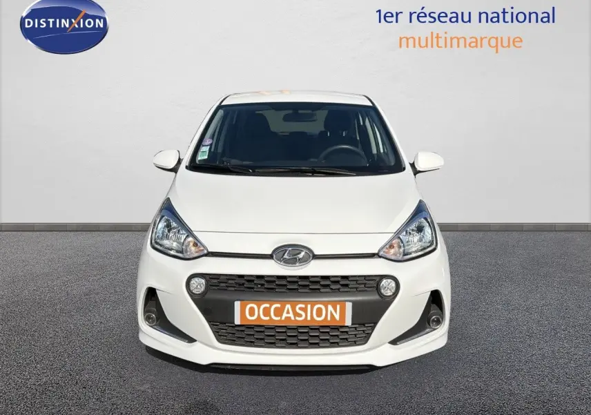 Vue de face d'une Hyundai i10 blanche 2018 avec calandre noire et plaque "OCCASION" orange visible.