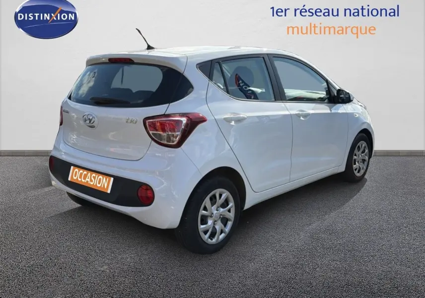 Vue 3/4 arrière droite d'une Hyundai i10 blanche 5 portes, avec feux arrière distinctifs et antenne de toit.
