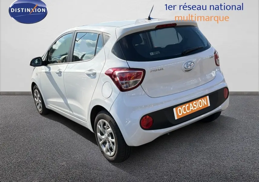Vue 3/4 arrière droite d'une Hyundai i10 blanche 2018, compacte avec hayon et feux arrière distinctifs.