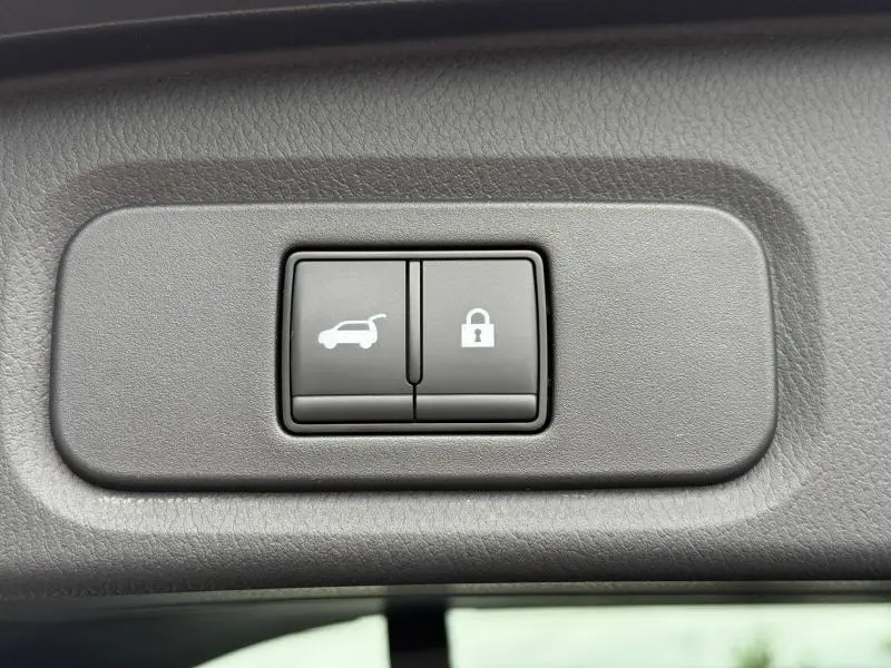Gros plan sur les boutons d'ouverture de coffre et de verrouillage intérieur du Nissan Qashqai gris argile 2025.