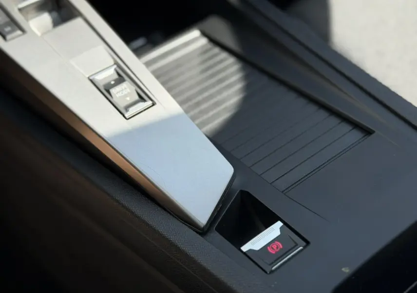 Gros plan sur la console centrale noire avec bouton frein de parking électrique et commande Drive Mode dans une Peugeot 308 gris Artense.