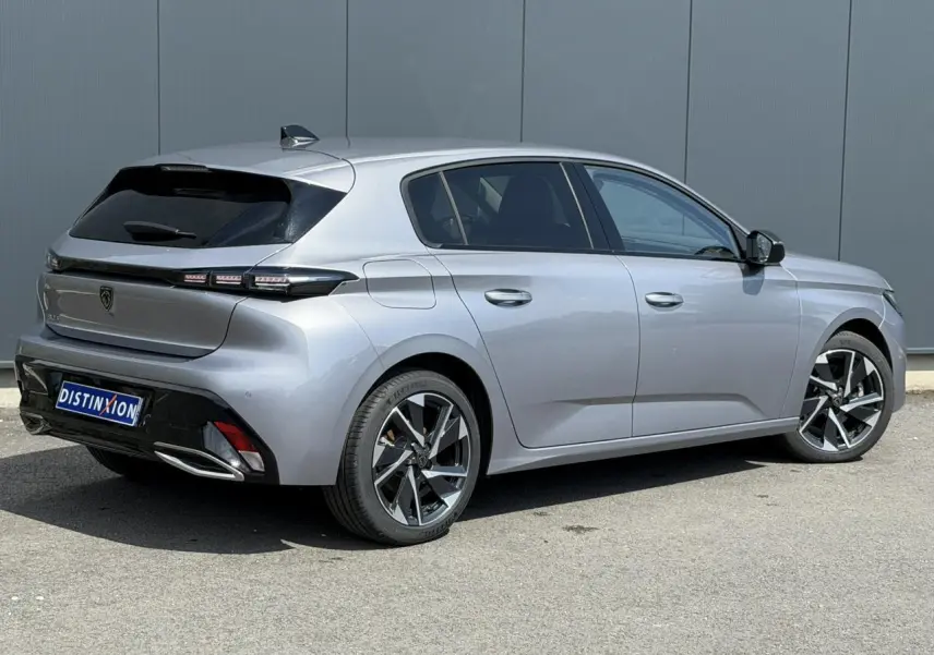 Vue 3/4 arrière droite de la Peugeot 308 2025 gris Artense avec jantes alliage 17'' et bandeau noir brillant arrière.