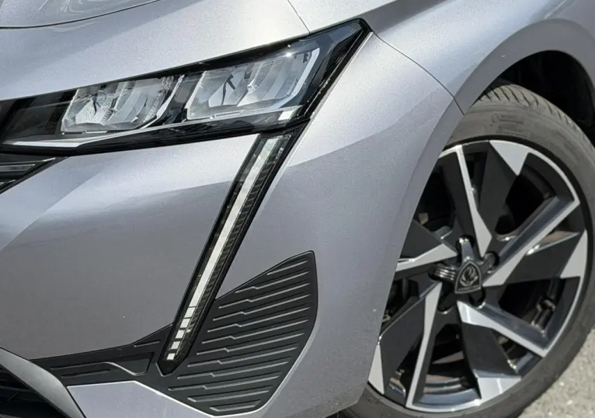 Gros plan sur l'avant droit gris Artense du Peugeot 308 2025, mettant en valeur le phare LED et la jante alliage 17 pouces.