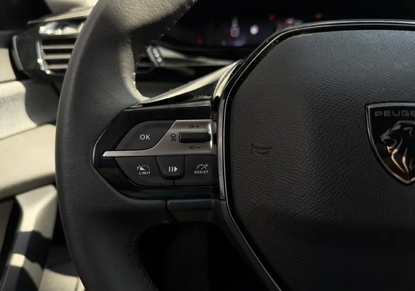 Gros plan sur le volant cuir noir de la Peugeot 308 2025, avec commandes du régulateur et logo lion central.