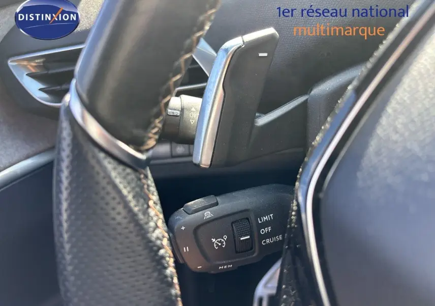 Gros plan sur la commande de régulateur de vitesse derrière le volant d’un Peugeot 5008 blanc nacré 2023.