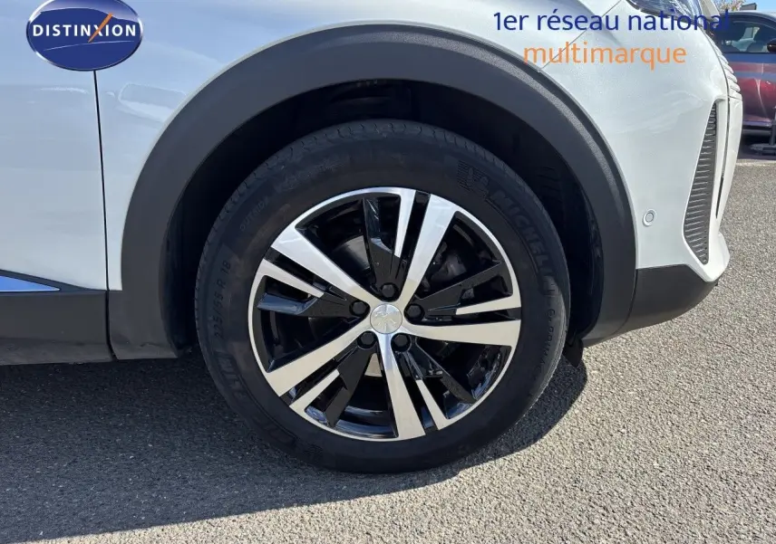 Gros plan sur la roue avant droite d’un Peugeot 5008 blanc nacré, mettant en valeur la jante alliage bicolore.