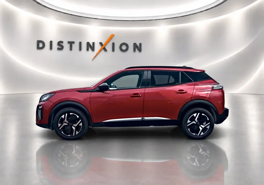 Profil droit du Peugeot 2008 rouge elixir 2025 avec jantes alu et toit noir dans un showroom lumineux.