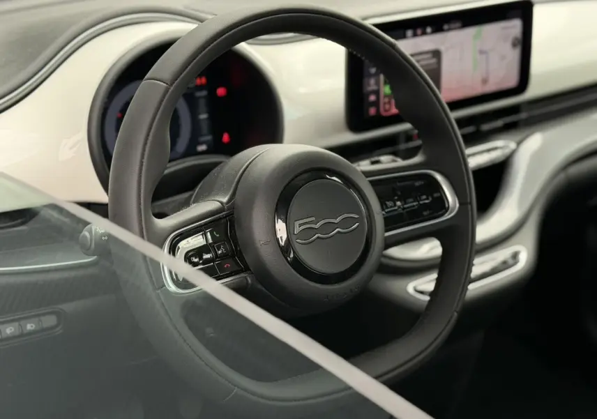 Vue rapprochée du volant noir Soft-Touch et du tableau de bord blanc Arctic de la Fiat 500 électrique 2024.