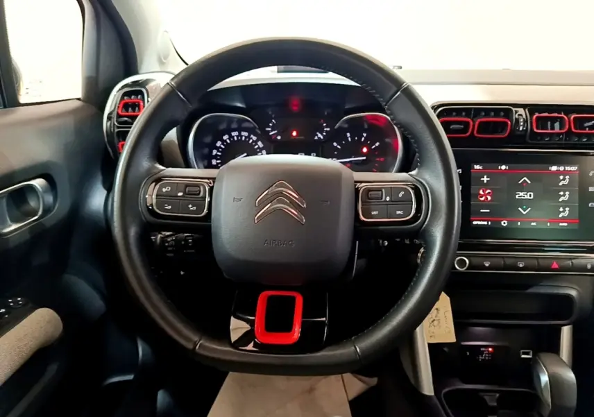 Vue intérieure centrée sur le volant cuir noir avec insert rouge et tableau de bord numérique du Citroën C3 Aircross.