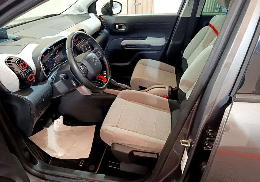 Intérieur avant droit d'une Citroën C3 Aircross 2020 avec sièges gris clair et touches rouges sur la console et aérateurs.