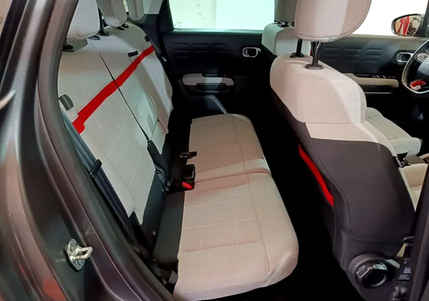 Vue intérieure arrière droite de la Citroën C3 Aircross 2020 avec sièges tissu gris clair et bande rouge distinctive.