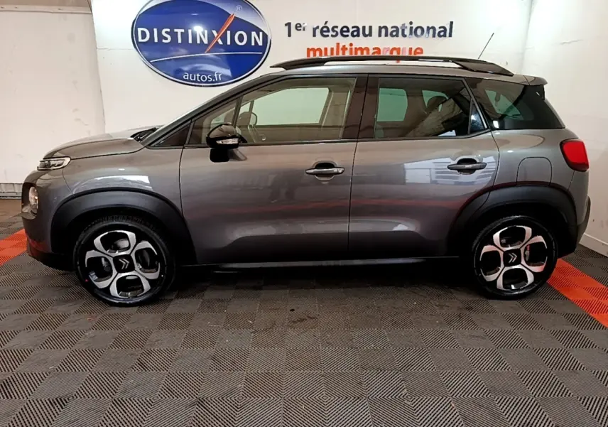 Profil côté gauche d'un Citroën C3 Aircross gris métallisé 2020 avec toit noir et jantes distinctives en intérieur showroom.