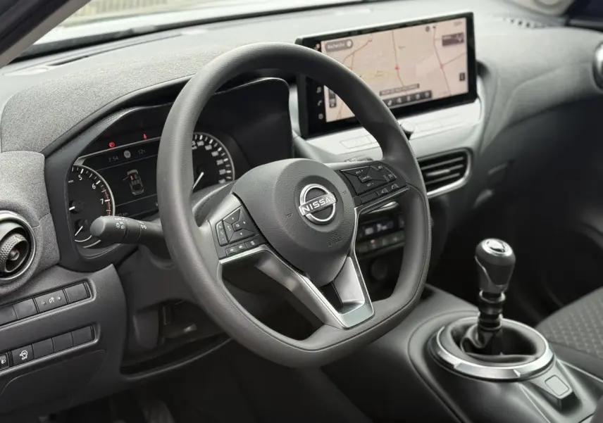 Vue intérieure centrée sur le volant Nissan et la console avec levier de vitesses manuelle et écran GPS tactile.