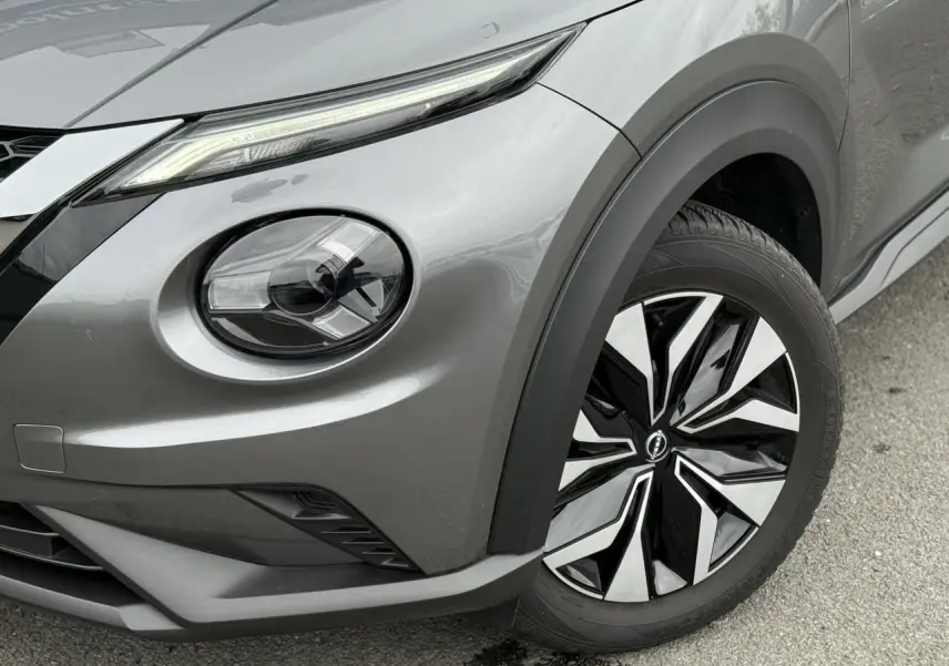 Gros plan sur l'avant droit du Nissan Juke 2025 gris foncé, mettant en valeur le phare rond et la jante bicolore.