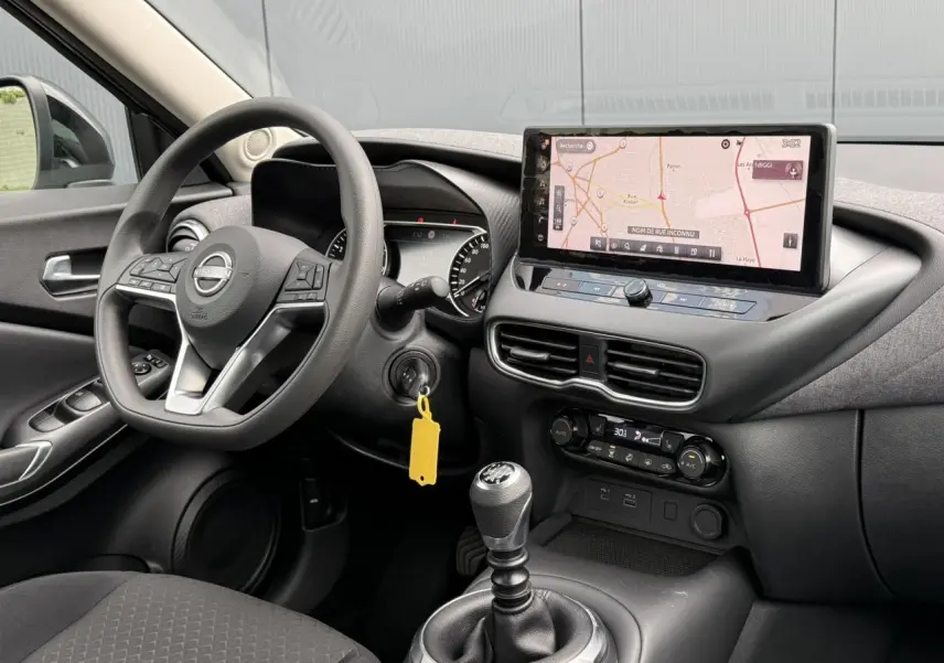 Vue intérieure côté conducteur du Nissan Juke 2025 gris, avec volant multifonctions et écran tactile GPS affiché.