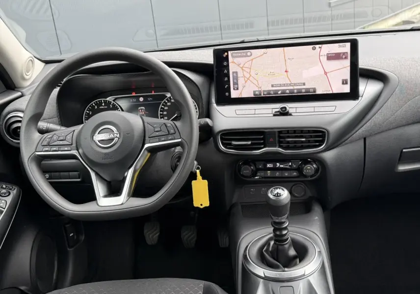 Vue intérieure avant du Nissan Juke 2025 gris foncé, mettant en valeur le volant multifonction et l'écran tactile GPS large.