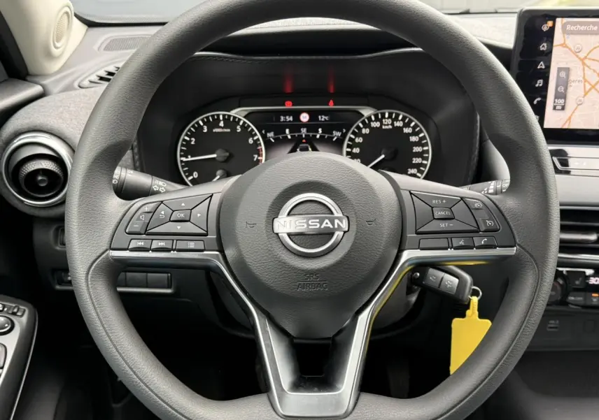 Vue centrée sur le volant noir du Nissan Juke 2025 avec commandes intégrées et écran GPS tactile visible à droite.
